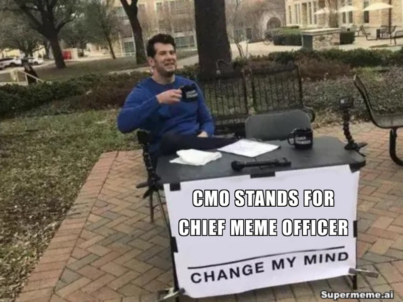 A man sits at an outdoor table with a sign reading CMO stands for Chief Meme Officer above Change my mind, with a Supermeme.ai watermark.